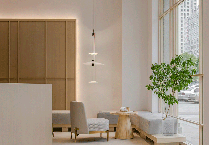 Recibidor de hotel de aspecto calmado con tonos suaves y madera clara en muebles y pared.